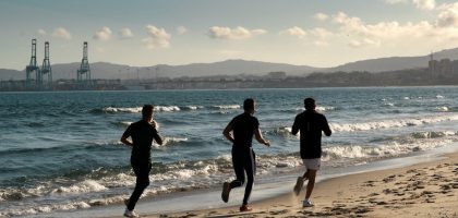 Three men jogging along a scenic beach, embracing a healthy lifestyle under a clear sky.